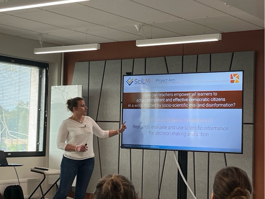 Näytöllä lukee “Project aim: How can teachers empower all learners to act as competent and effective democratic citizens in a world flooded by socio-scientific mis- and disinformation? PISA 2025 Science Competency 3: research, evaluate and use scientific information for decision making and action”